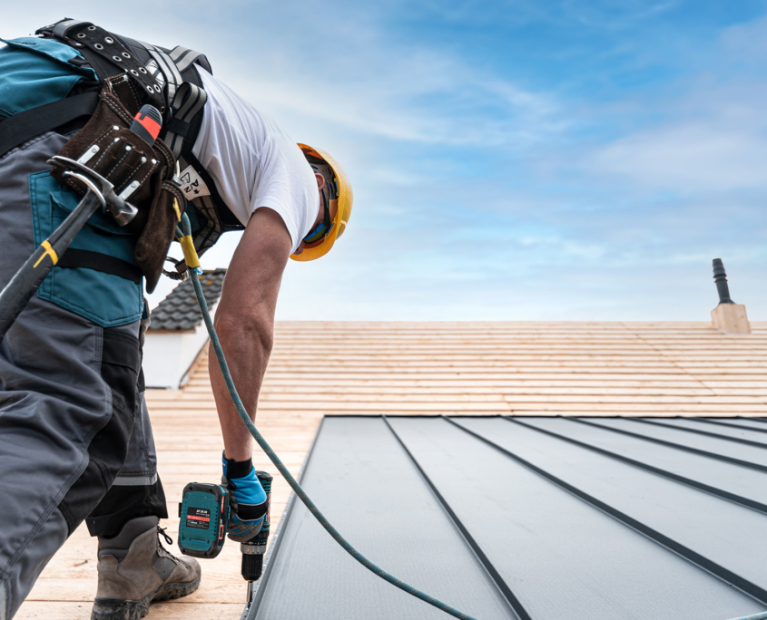 A Roofer With A Safety Harness And Tool Belt Is Working With A Electric Screwdriver On The Roof